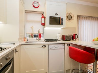 A kitchen with white cabinets red clock red appliances and a red bar stool at Church View in Ambleside