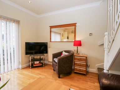 A living area with a TV on a stand a chair a side table with a lamp and a mirror on the wall at Church View in Ambleside