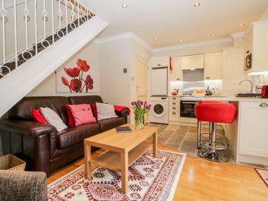 An open plan living room and kitchen with a brown leather sofa and red stools at Church View in Ambleside
