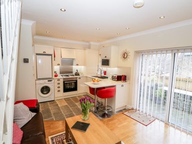 A kitchen and living area with white cabinets red bar stools and a coffee table with flowers at Church View in Ambleside