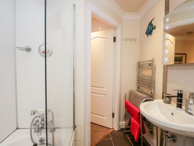 A bathroom with a shower, white sink, towel racks with towels, and an open door at Church View in Ambleside