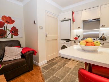 A kitchen and living area with a bowl of fruit on a counter a brown leather couch with cushions and a red throw blanket at Church View in Ambleside