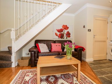 A seating area with a brown leather sofa cushions a wooden coffee table and a vase of flowers under stairs at Church View in Ambleside