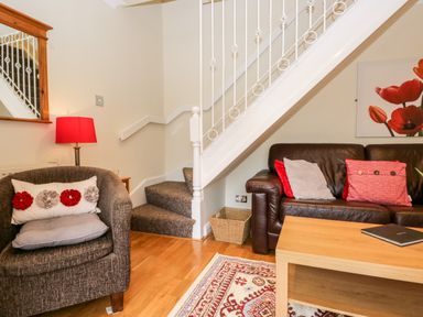 A living room with a brown armchair a brown leather sofa and a wooden coffee table under a staircase at Church View in Ambleside