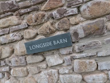 A stone wall with a plaque reading Longside Barn in Gilwern