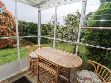 A small enclosed porch with a wicker table and two wicker chairs with cushions at Bryn yr Haf in Llanfair Clydogau near Lampeter