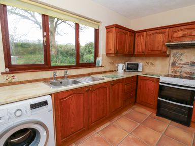 A kitchen with wooden cabinets, a washing machine, a sink, a microwave, a kettle, and a stove with a tiled backsplash at Bryn yr Haf in Llanfair Clydogau near Lampeter