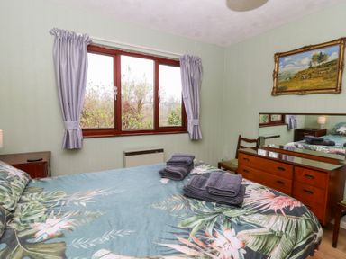 A bedroom with a bed with floral bedding beside a window with purple curtains at Bryn yr Haf in Llanfair Clydogau near Lampeter