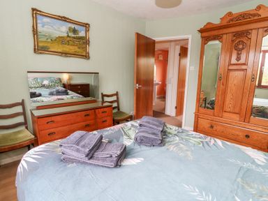 A bedroom with a bed, wooden dresser with mirror, two chairs, wooden wardrobe and an open door showing a bathroom at Bryn yr Haf in Llanfair Clydogau near Lampeter