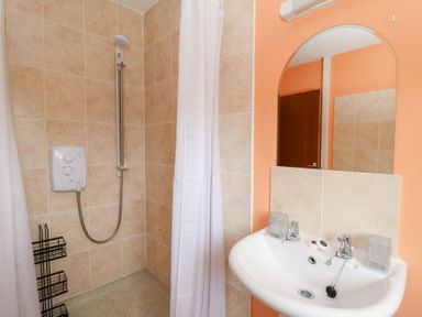 A bathroom with a shower area with beige tiles a white shower curtain a white sink with two taps and a mirror above at Bryn yr Haf Llanfair Clydogau near Lampeter