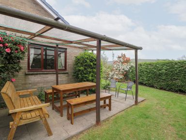 An outdoor patio with wooden bench seating a wooden table two metal chairs and plants at Bryn yr Haf Llanfair Clydogau near Lampeter