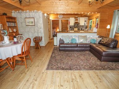 A living room with a brown leather sectional sofa and a dining table with wooden chairs at Y Caban in Llechwedd The Conwy Valley