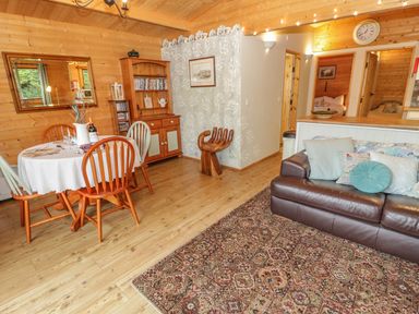 A wooden dining area with table and chairs next to a brown leather sofa and hallway at Y Caban in Llechwedd The Conwy Valley