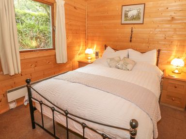 A bedroom with a metal bed frame white bedding two bedside tables with lamps and wooden walls at Y Caban in Llechwedd The Conwy Valley