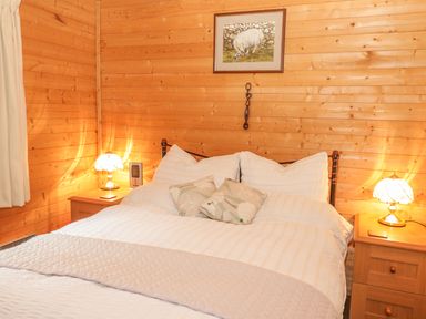 A bedroom with a double bed bedside tables with lamps wooden walls and a framed picture at Y Caban in Llechwedd The Conwy Valley