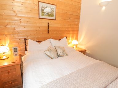 A bedroom with a double bed linens pillows bedside tables with lamps and a wooden wall with a painting at Y Caban in Llechwedd The Conwy Valley