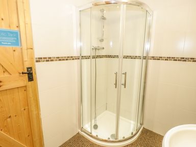 A corner shower with glass doors in a bathroom with tiled walls and a wooden door at Y Caban in Llechwedd The Conwy Valley