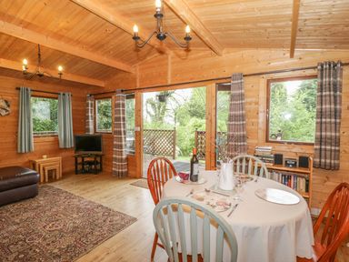 A wooden interior dining and living area with a round dining table set with plates and wine at Y Caban in Llechwedd The Conwy Valley