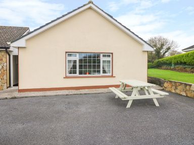 An exterior view of a beige house with a window and a white picnic table on a paved area at Island View in Ardmore County Waterford