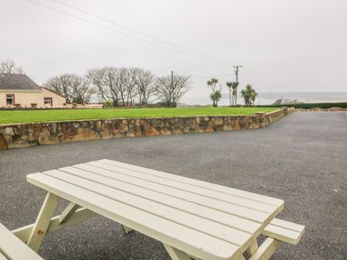 An outdoor area with a white picnic table a stone wall green grass trees and a house in the background at Island View in Ardmore County Waterford