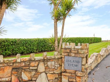 A stone wall with a sign reading Island View beside a trimmed hedge and palm trees at Island View in Ardmore County Waterford