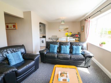 A living room with black leather sofas blue cushions a wooden coffee table and a dining table with flowers at Island View in Ardmore County Waterford