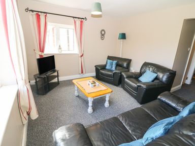 A living room with black leather sofas blue cushions a wooden coffee table a flat screen tv on a black stand and curtains with red stripes at Island View in Ardmore County Waterford