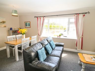 A living room with a black leather sofa with blue cushions a wooden dining table with white chairs and yellow flowers on top at Island View in Ardmore County Waterford