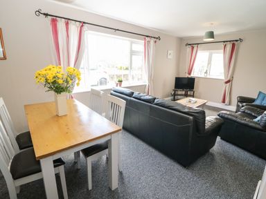 A living room with black leather sofas dining table with yellow flowers and windows with red and white curtains at Island View in Ardmore County Waterford