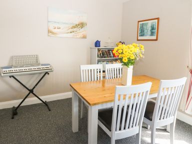 A dining room with a wooden table and four white chairs a keyboard on a stand bookshelf with books and a vase of yellow flowers on the table at Island View in Ardmore County Waterford