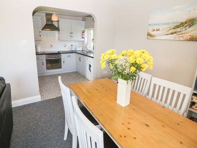 A dining area with a wooden table and white chairs with flowers on the table next to a kitchen with grey cabinets and appliances at Island View in Ardmore County Waterford