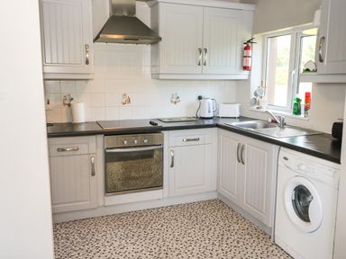 A kitchen with white cabinets a black countertop a stove oven washing machine kettle toaster and a window at Island View in Ardmore County Waterford