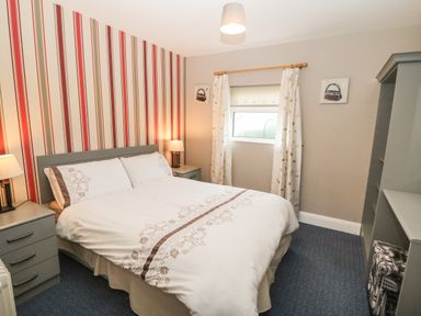 A bedroom with a double bed two bedside tables and lamps striped wallpaper and a window with curtains at Island View in Ardmore County Waterford