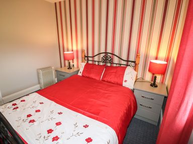 A bedroom with a red bedspread two bedside tables with red lamps and striped wallpaper at Island View in Ardmore County Waterford