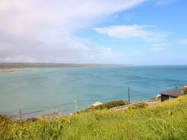 A grassy hill overlooking a coastal road, houses, and a large body of water under a partly cloudy sky at Island View in Ardmore County Waterford