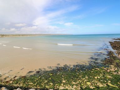 A beach with sandy shore and rocks covered with seaweed and a coastline in the distance at Island View in Ardmore County Waterford