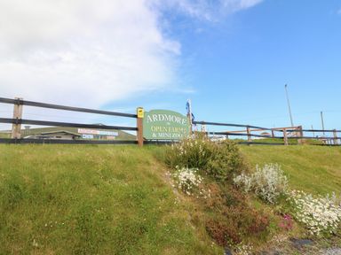A grassy slope with flowers and a fence with a sign for Ardmore Open Farm and Mini Zoo in Ardmore County Waterford