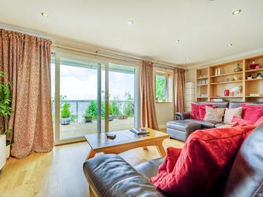 A living room with leather sofas and red cushions near sliding glass doors with patterned curtains at Solway Cottage in Bowness-on-Solway near Wigton