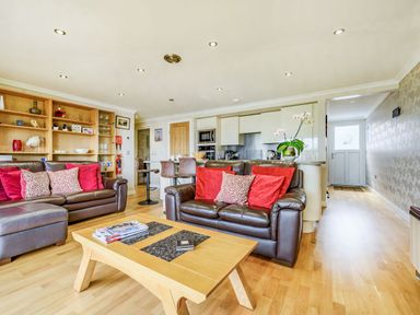 A living room with brown leather sofas red cushions a wooden coffee table and an open kitchen with bar stools at Solway Cottage in Bowness-on-Solway near Wigton