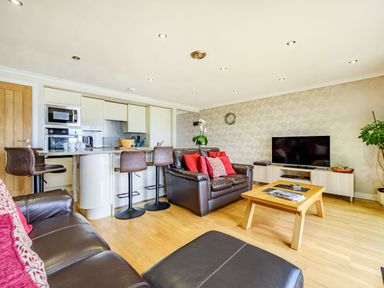 An open plan living area with a kitchen island and bar stools and leather sofas and a wooden coffee table and a television at Solway Cottage in Bowness-on-Solway near Wigton