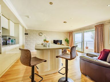 A kitchen and living area with high stools at a kitchen island and sliding glass doors leading to a deck at Solway Cottage in Bowness-on-Solway near Wigton