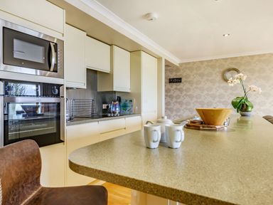 A kitchen with built in microwave oven cabinets countertop with cups and a teapot and a flower vase at Solway Cottage in Bowness-on-Solway near Wigton