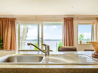 A kitchen sink with a faucet in front of windows with curtains at Solway Cottage in Bowness-on-Solway near Wigton