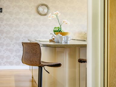 A kitchen island with a brown leather chair white teapot and mugs and a vase with flowers on the counter at Solway Cottage in Bowness-on-Solway near Wigton