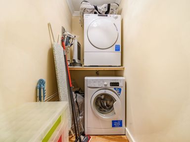 A laundry area with a washing machine and dryer with an ironing board and cleaning tools at Solway Cottage in Bowness-on-Solway near Wigton
