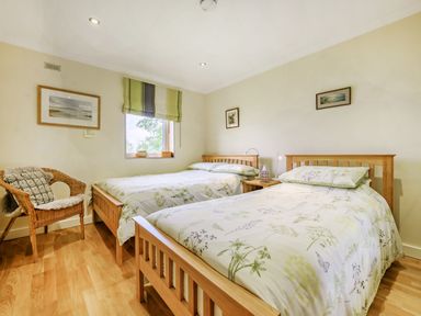 A bedroom with two wooden single beds a wicker chair and framed pictures on the walls at Solway Cottage in Bowness-on-Solway near Wigton