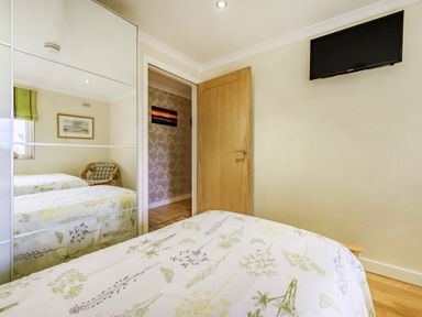 A bedroom with a bed covered by a floral duvet a chair beside a window and a wall-mounted television at Solway Cottage in Bowness-on-Solway near Wigton