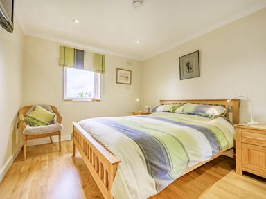 A bedroom with a wooden double bed, striped bedding, a wicker chair, and a window at Solway Cottage in Bowness-on-Solway near Wigton