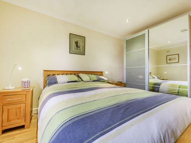 A bedroom with a double bed with striped bedding two bedside tables with lamps and a wardrobe with sliding mirrored doors at Solway Cottage in Bowness-on-Solway near Wigton