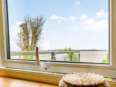 A view through a window showing a tree a glass balcony railing and a landscape in the distance at Solway Cottage in Bowness-on-Solway near Wigton